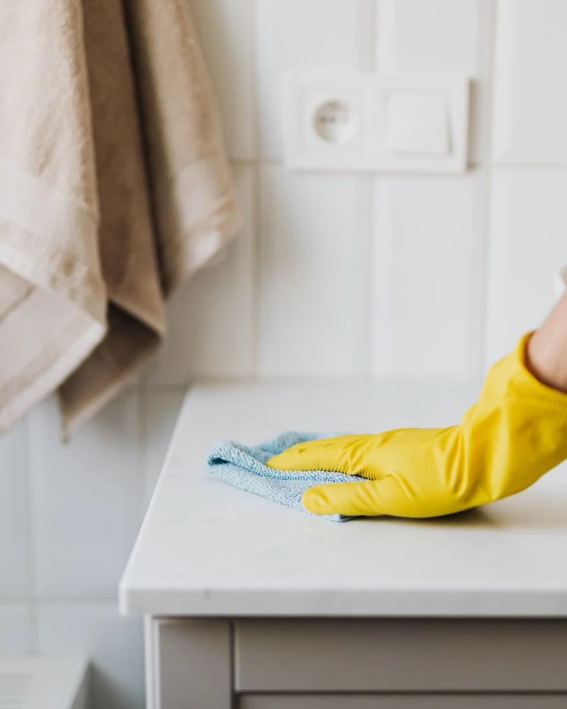 Eine Hand mit gelbem Handschuh reinigt eine Waschtischoberfläche.